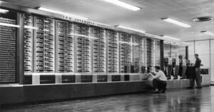a large early computer that is the size of a room with rows of punch cards and ticker tape
